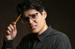 man wearing black denim jacket holding pencil and yellow sticky notes standing while showing confused reaction